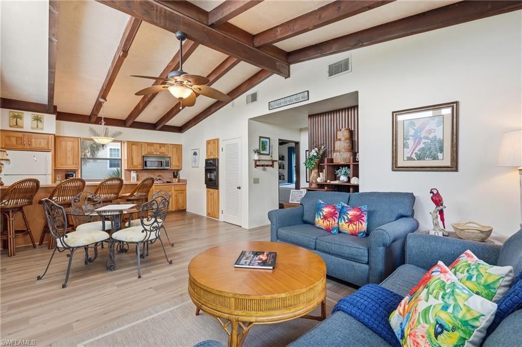 Open-concept living space with a vaulted ceiling featuring exposed wood beams and a ceiling fan - Virtually Edited Image