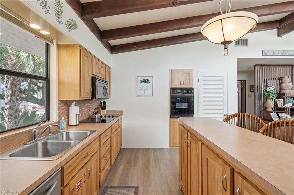 Kitchen with wood-finish cabinetry, integrated built-in appliances, and sloped ceiling with exposed beams - Virtually Edited Image