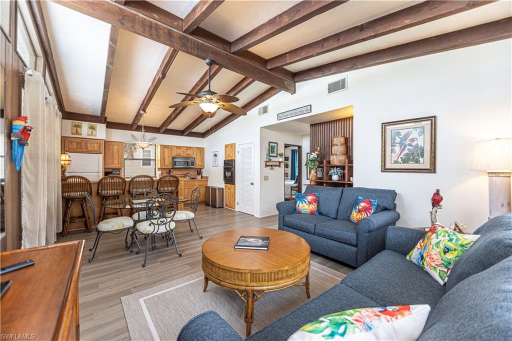 Living area featuring wood-finish flooring, vaulted ceilings with exposed wood beams, and a ceiling fan - Virtually Edited Image