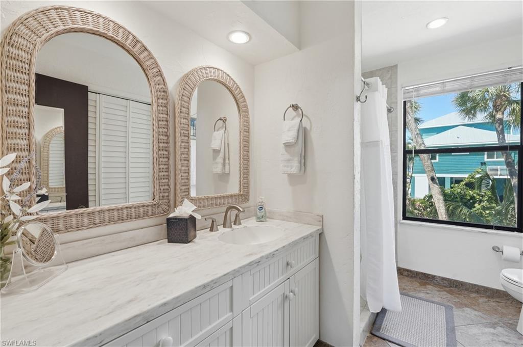 Bathroom featuring a dual vanity with white beadboard cabinetry, a light-toned countertop, and two arch-top mirrors with woven frames - Virtually Edited Image