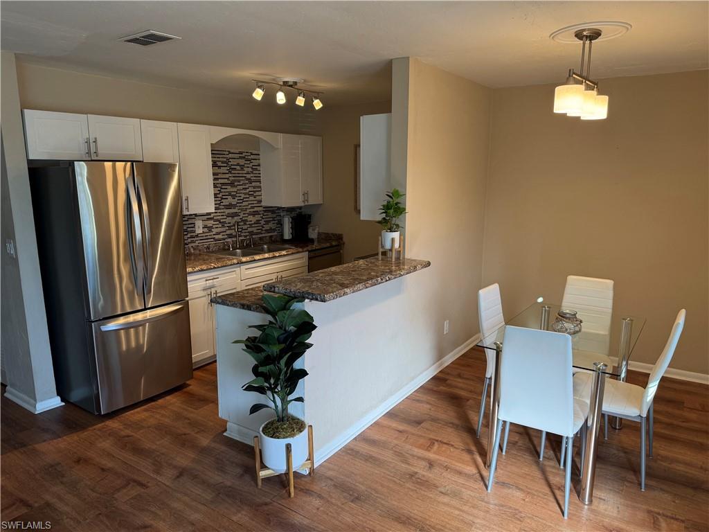 Kitchen with appliances with stainless steel finishes, dark stone countertops, white cabinetry, tasteful backsplash, and a peninsula