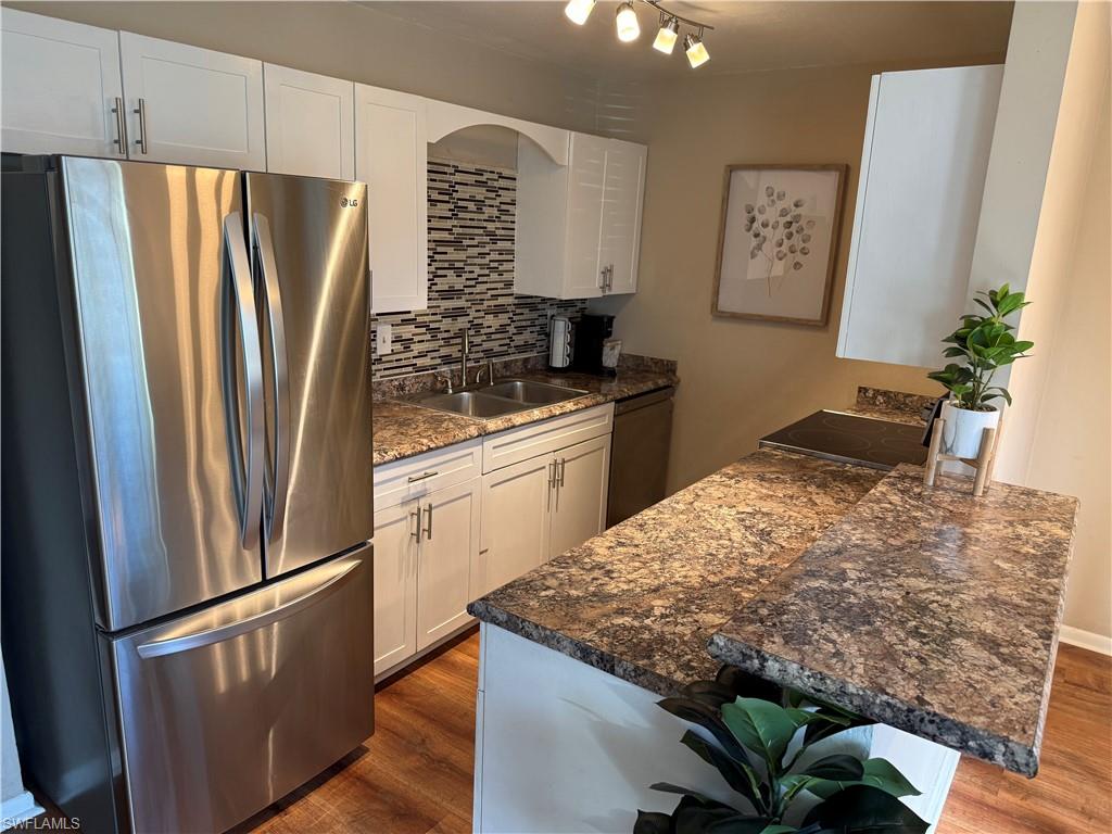 Kitchen featuring appliances with stainless steel finishes, decorative backsplash, white cabinets, dark stone countertops, and a peninsula