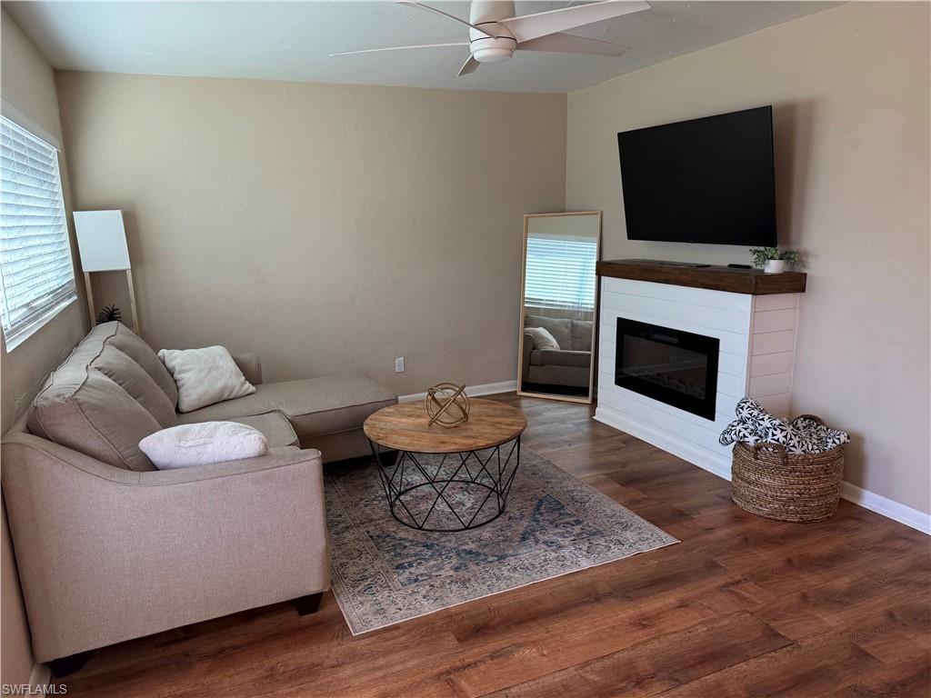 Living area with a glass covered fireplace, a ceiling fan, dark wood-style floors, and healthy amount of natural light