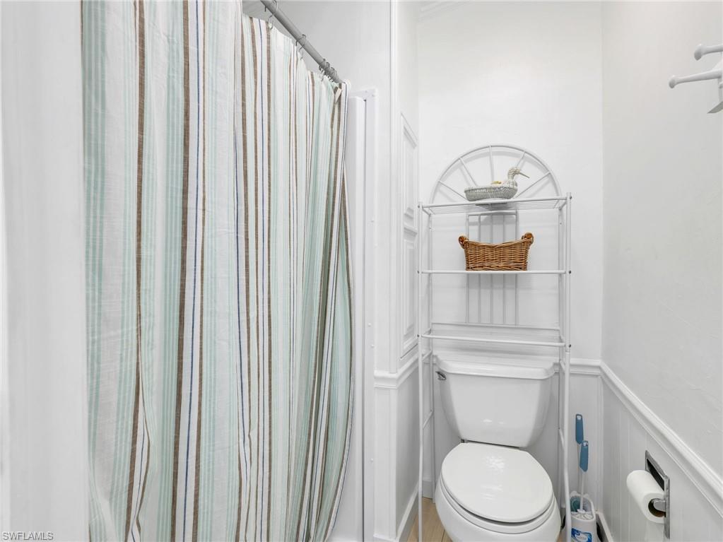 Bathroom featuring a white toilet, white wainscoting, and a shower with a striped curtain
