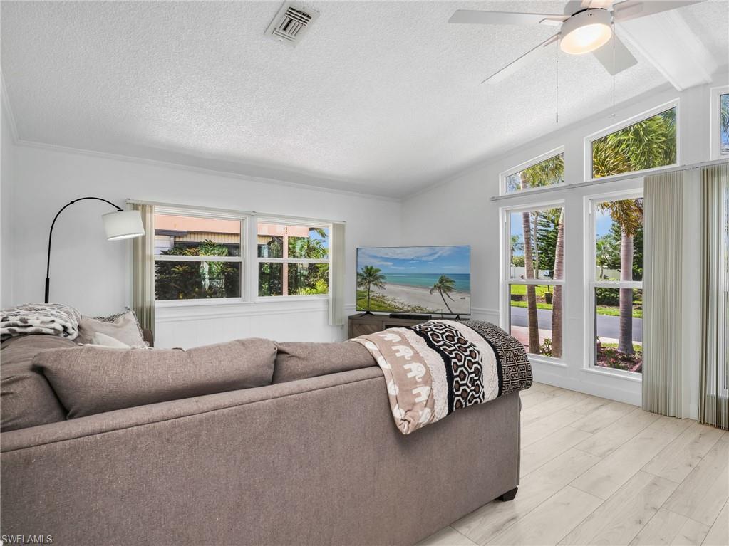 Vaulted ceiling living area featuring light wood-finish flooring, multiple large windows, and a ceiling fan with integrated lighting