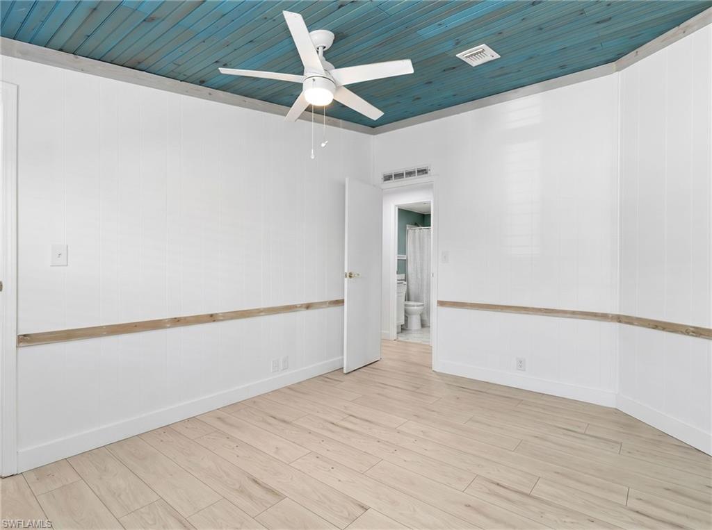 Room featuring wood-finish flooring, white vertical wall paneling, a distinctive blue-toned plank ceiling, and a ceiling fan