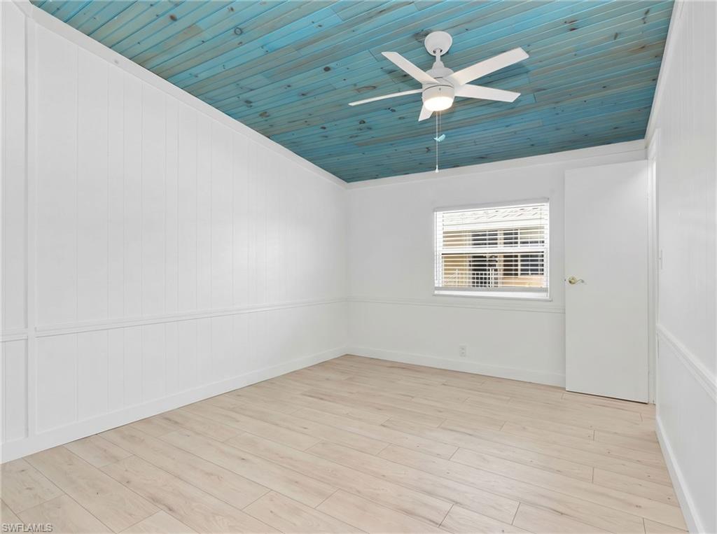 Room featuring a vibrant blue wood-paneled ceiling with a white ceiling fan, light wood-finish flooring, white paneled walls, and a window with horizontal blinds