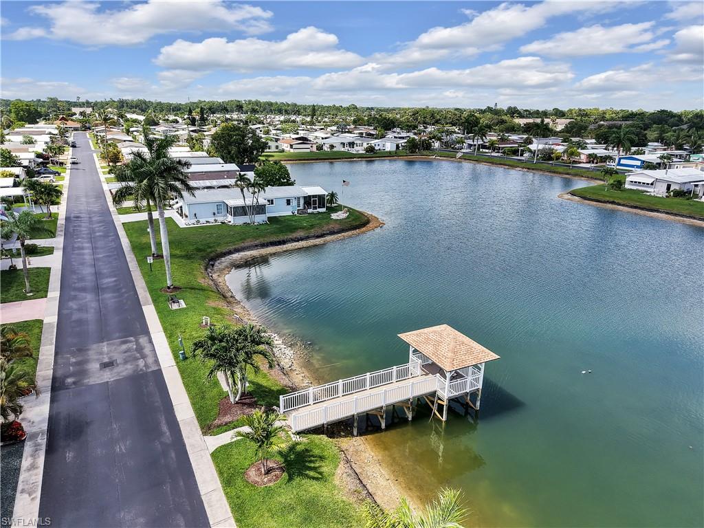 Waterfront property featuring a covered dock, mature palm trees, manicured lawn, and paved roadways