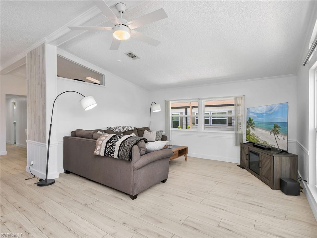 Open living area featuring wood-finish flooring, white walls, and a ceiling fan with integrated lighting