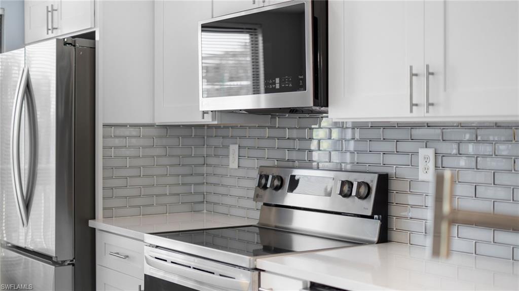 Kitchen with appliances with stainless steel finishes, decorative backsplash, white cabinets, and light stone countertops