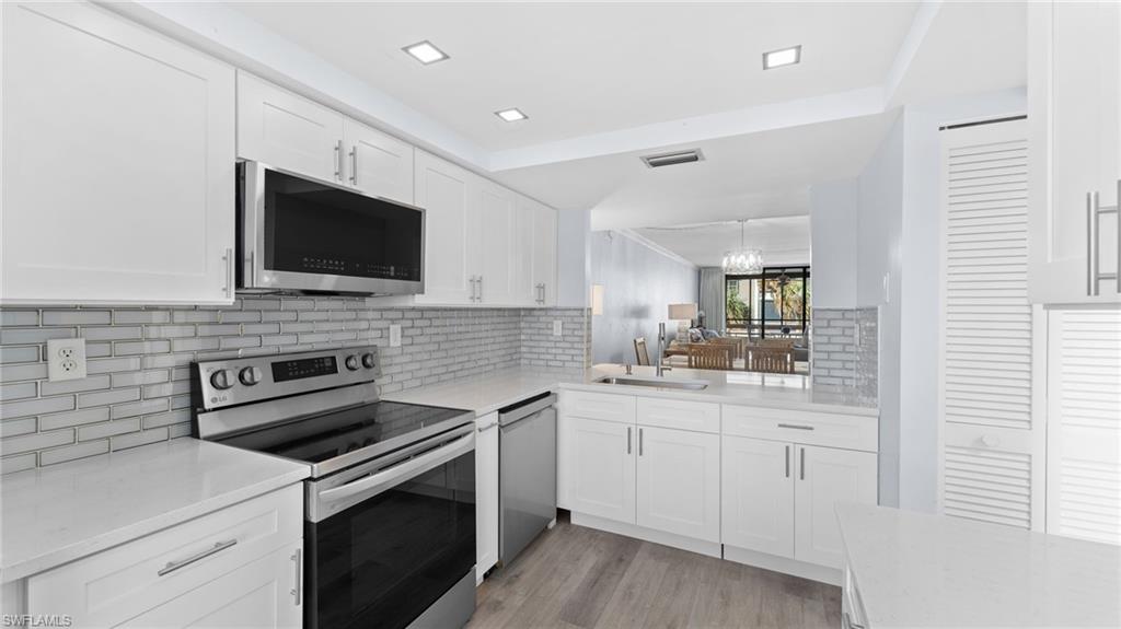 Kitchen with appliances with stainless steel finishes, white cabinetry, light stone counters, and backsplash