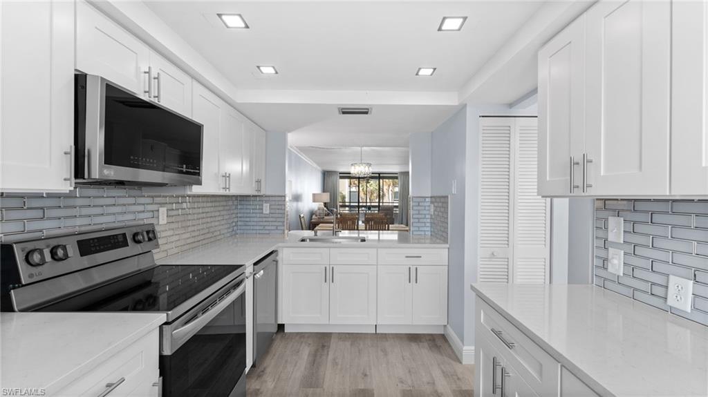 Kitchen featuring appliances with stainless steel finishes, light stone countertops, and white cabinetry