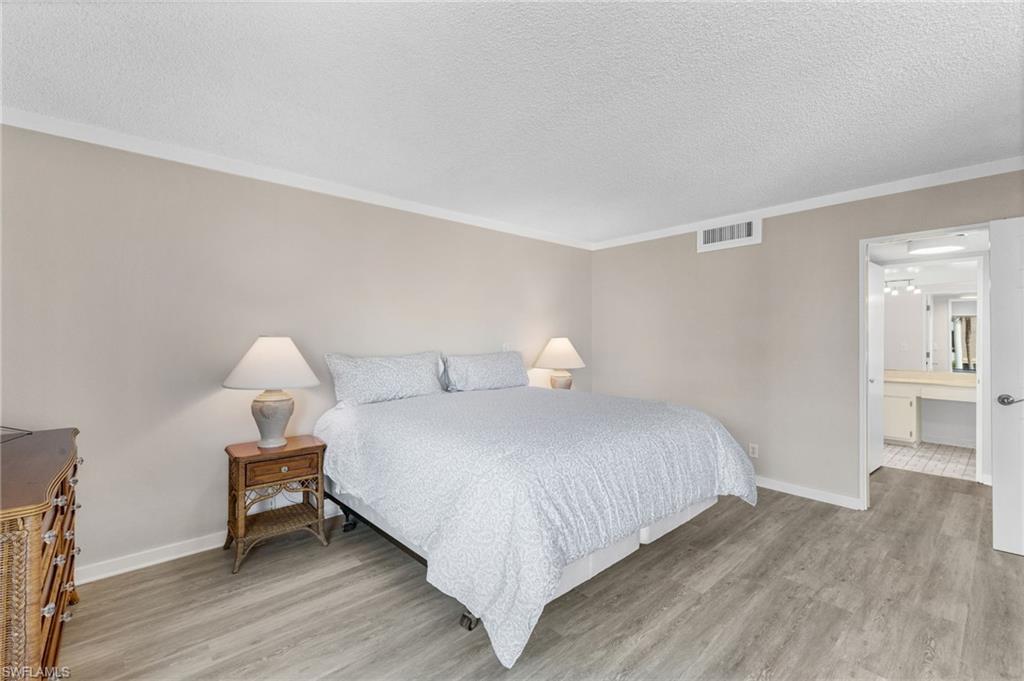 Bedroom featuring a textured ceiling, light wood-style floors, ensuite bath, and crown molding