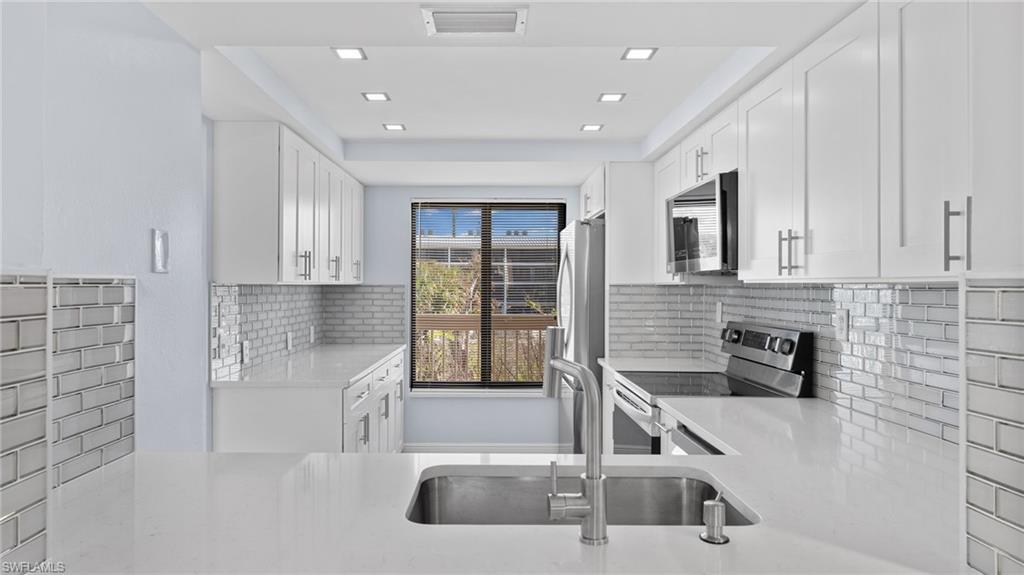 Kitchen with appliances with stainless steel finishes, white cabinets, light stone countertops, tasteful backsplash, and recessed lighting