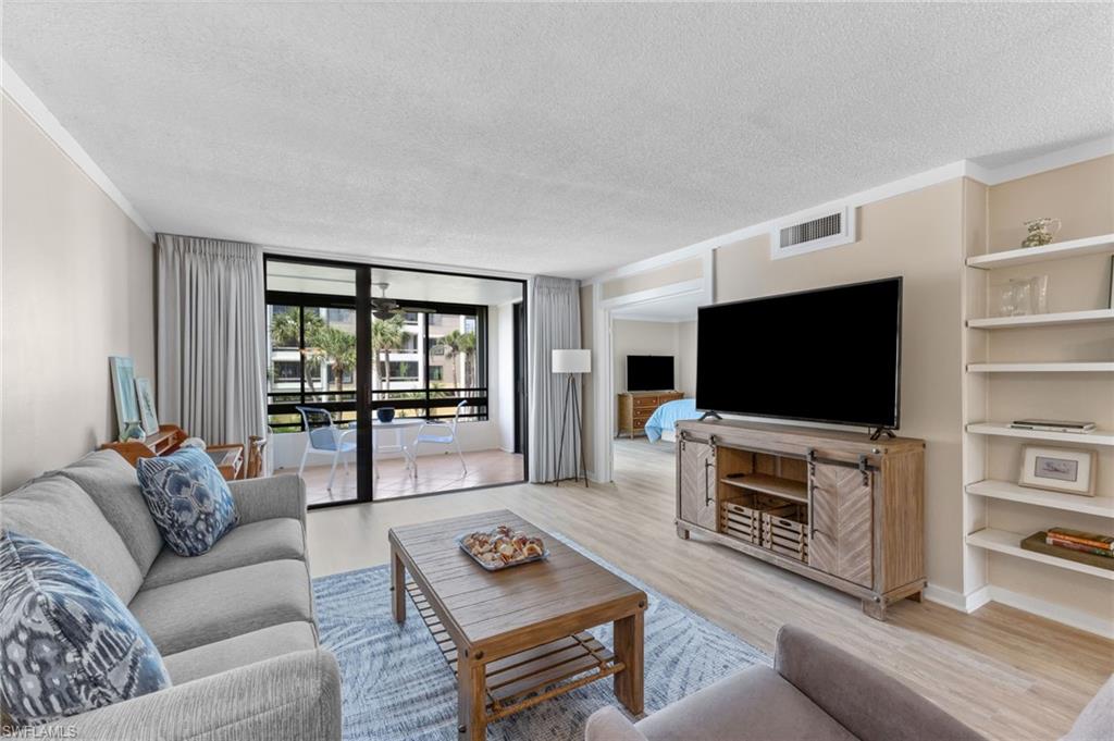 Living room featuring a wall of windows, a textured ceiling, wood finished floors, built in features, and crown molding