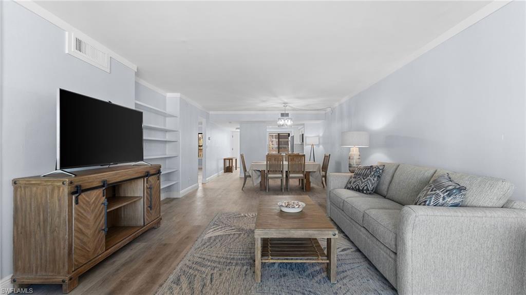 Living area with built in shelves, wood finished floors, and ornamental molding