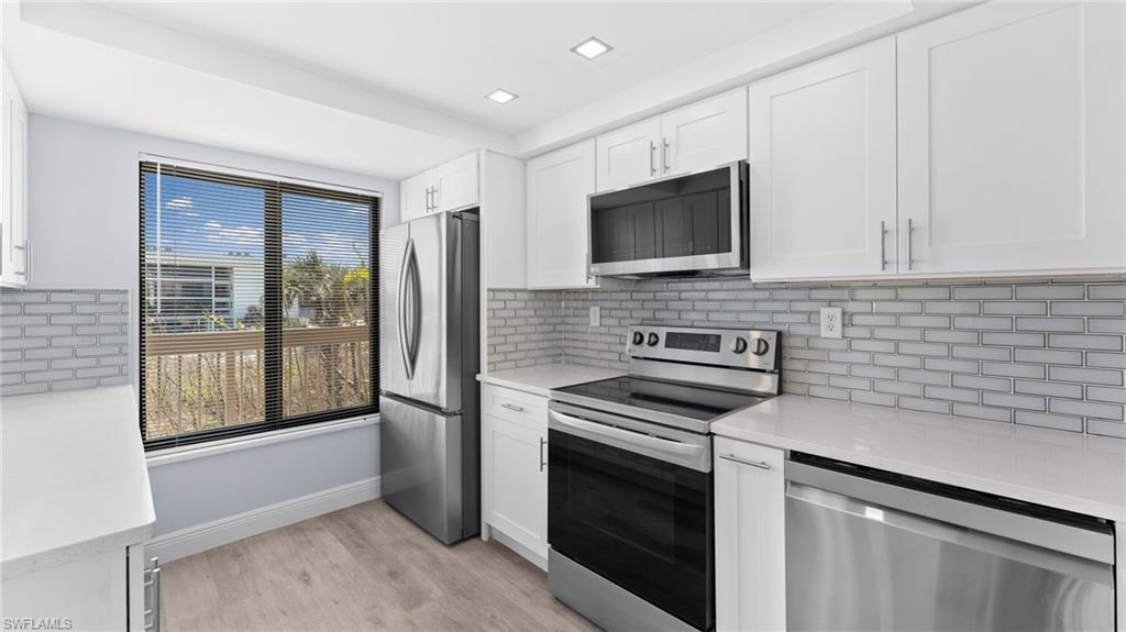 Kitchen featuring appliances with stainless steel finishes, light stone counters, white cabinets, and tasteful backsplash