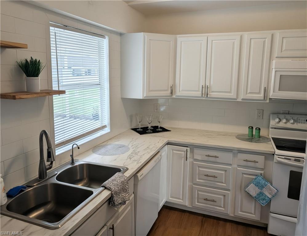 Kitchen featuring white cabinetry, white subway tile backsplash, light-toned countertops, a double basin stainless steel sink with a gooseneck faucet, and wood-finish flooring