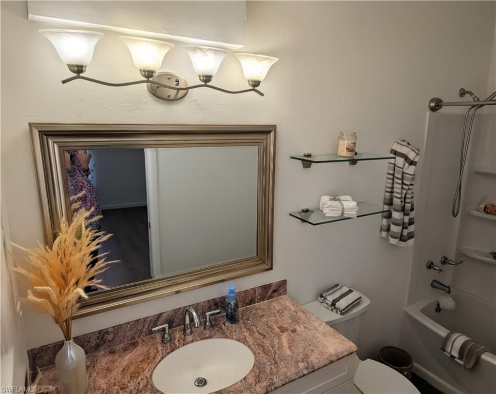Bathroom vanity featuring a framed mirror, four-light fixture, and a countertop with an integrated sink