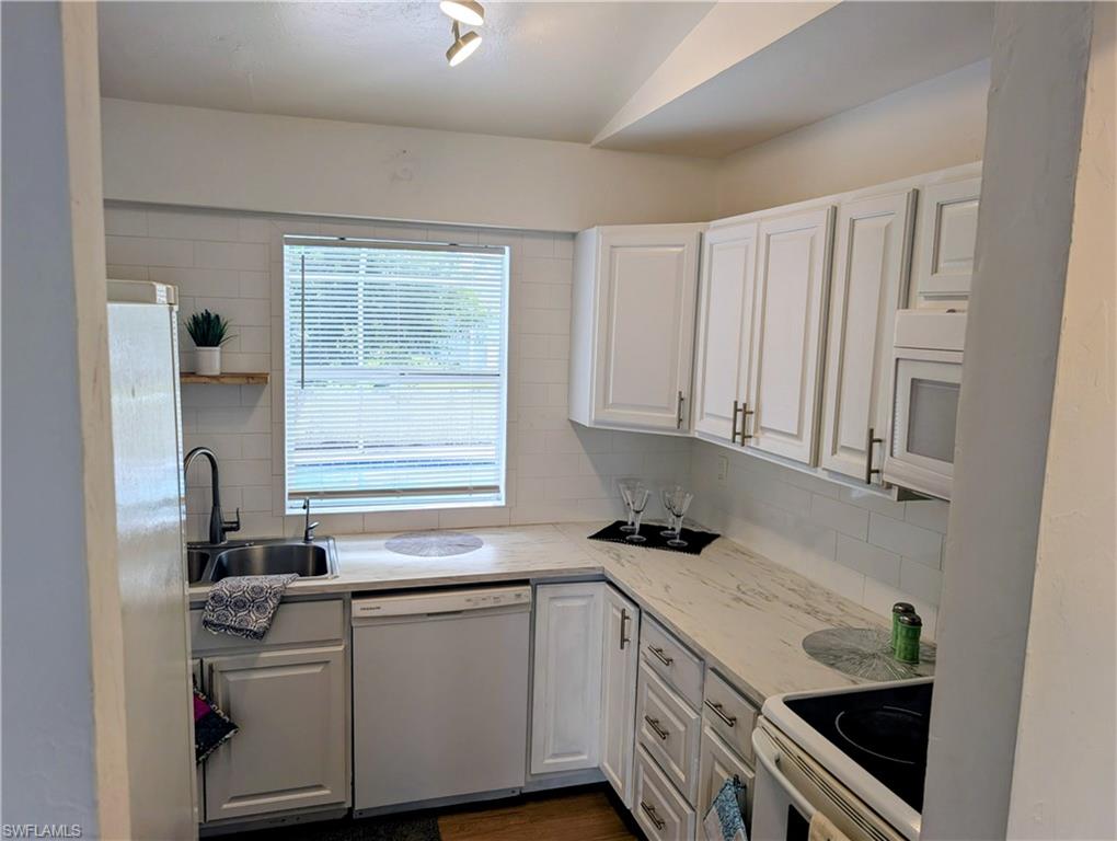 Kitchen featuring white cabinetry, light-toned countertops, subway tile backsplash, and stainless steel sink with a matte black faucet