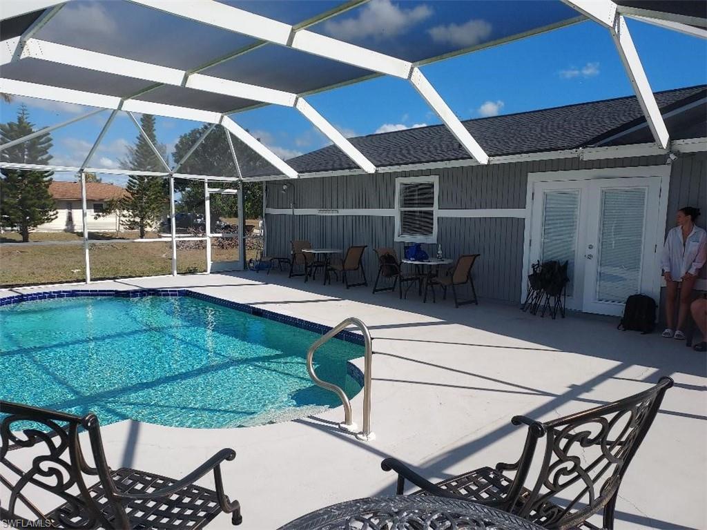 Screened-in pool deck featuring a kidney-shaped pool with a blue tile border, concrete decking, and direct access to the home via double French doors