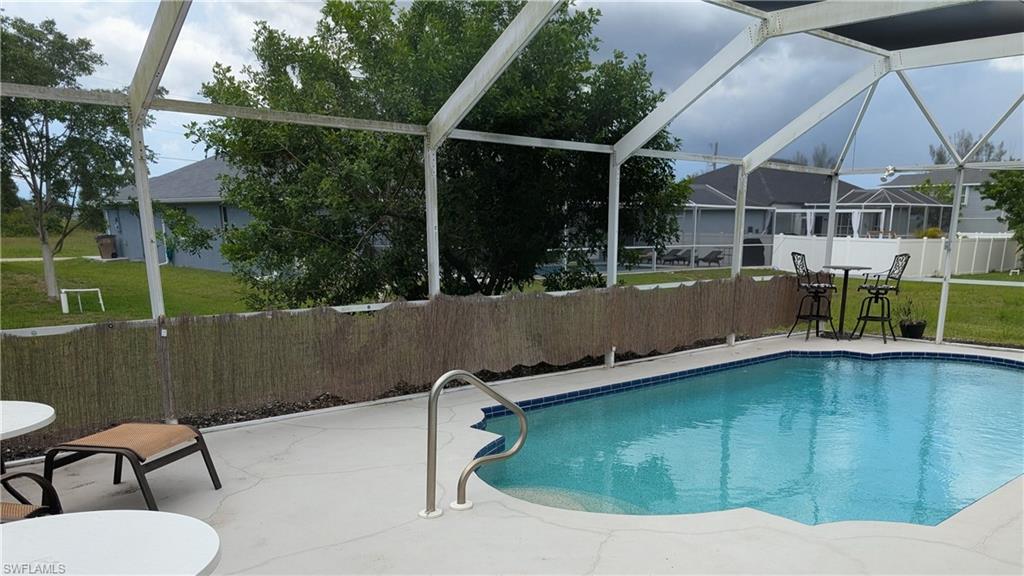 Screened-in outdoor living space featuring an in-ground swimming pool with blue tile trim, a concrete pool deck, and a bamboo privacy screen