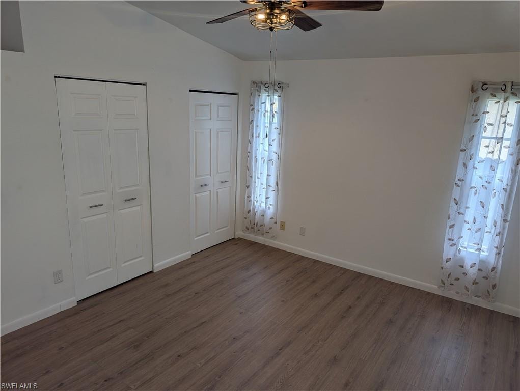 Spacious room featuring wood-finish flooring, two bi-fold door closets, vaulted ceilings, and a ceiling fan with integrated lighting