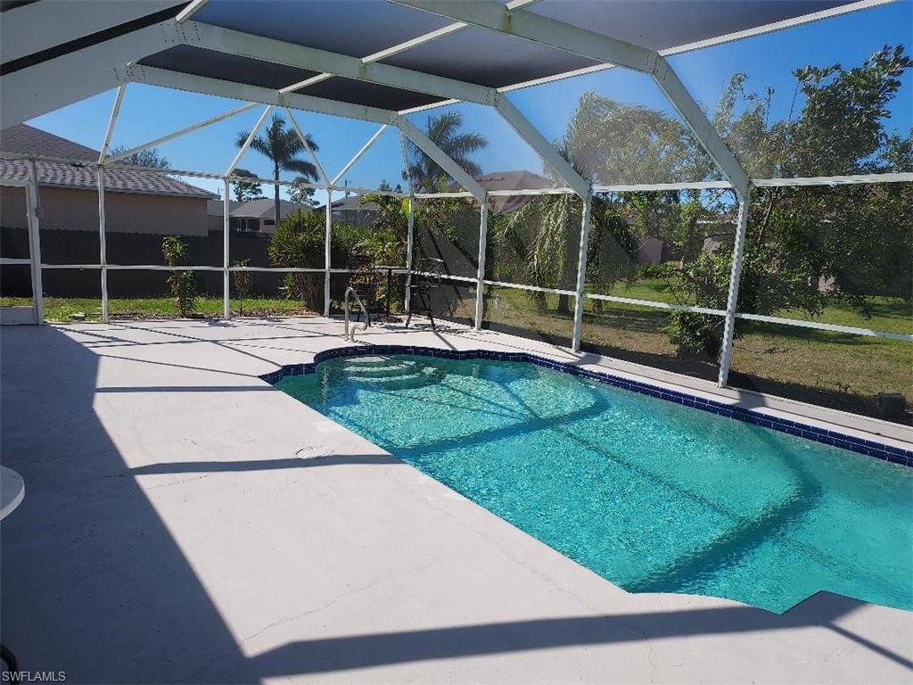 Screened enclosure featuring a freeform swimming pool with integrated steps, a surrounding concrete deck, and a metal handrail