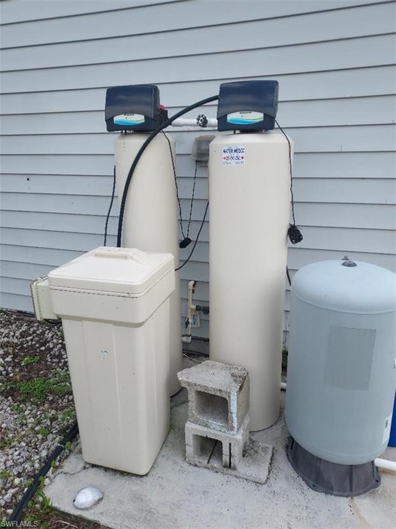 Exterior utility area featuring two water treatment tanks, a water softener unit, and a pressure tank, all resting on a concrete pad
