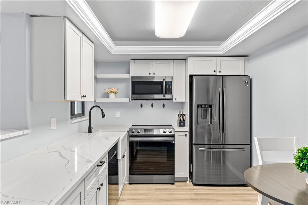 Kitchen with light hardwood / wood-style floors, a raised ceiling, light stone countertops, white cabinets, and appliances with stainless steel finishes