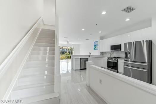 Kitchen with appliances with stainless steel finishes, white cabinetry, recessed lighting, a peninsula, and light countertops