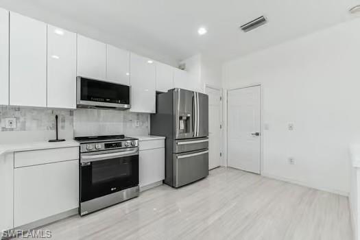Kitchen featuring appliances with stainless steel finishes, white cabinets, light countertops, backsplash, and light wood-style flooring