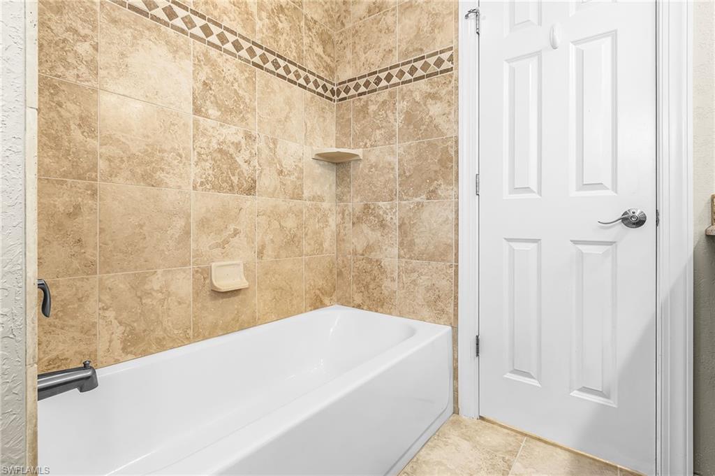 Bathroom featuring a white bathtub, light-toned tile surround with decorative accent band, and a built-in corner shelf