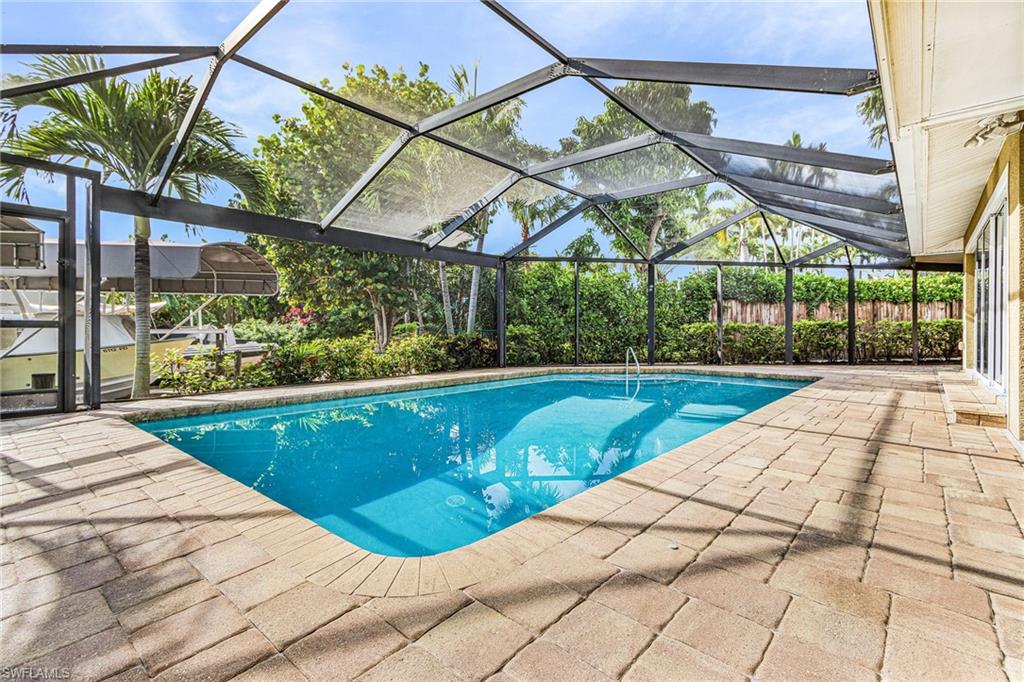 Screened swimming pool enclosure featuring a rectangular pool, paver deck, and lush perimeter landscaping