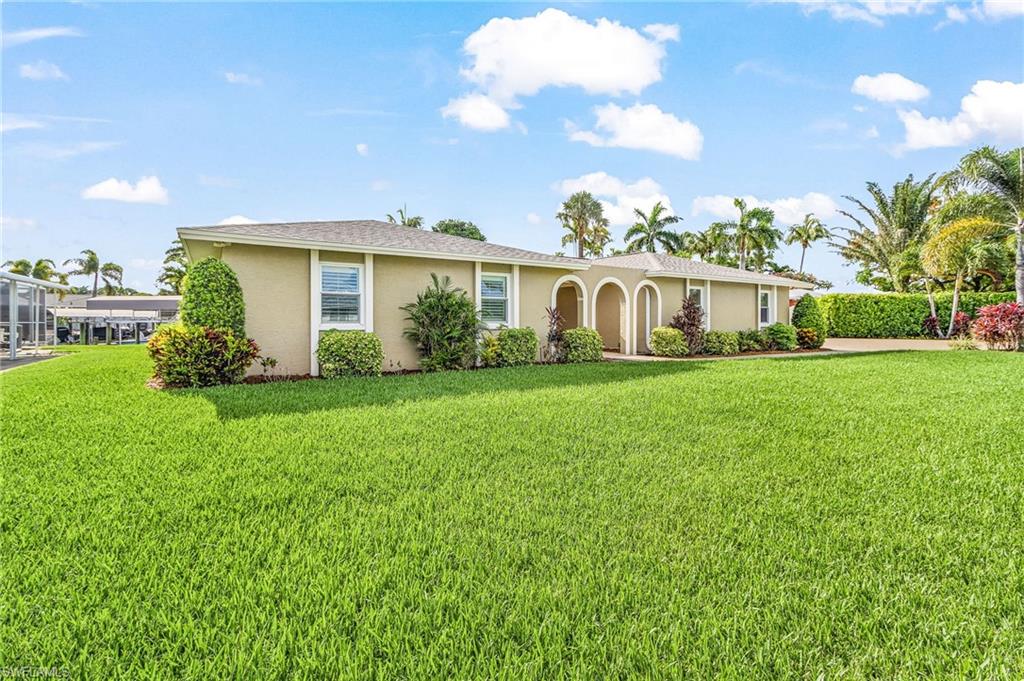Expansive green lawn with a single-story residence featuring a tan exterior, multiple windows, and an arched entry