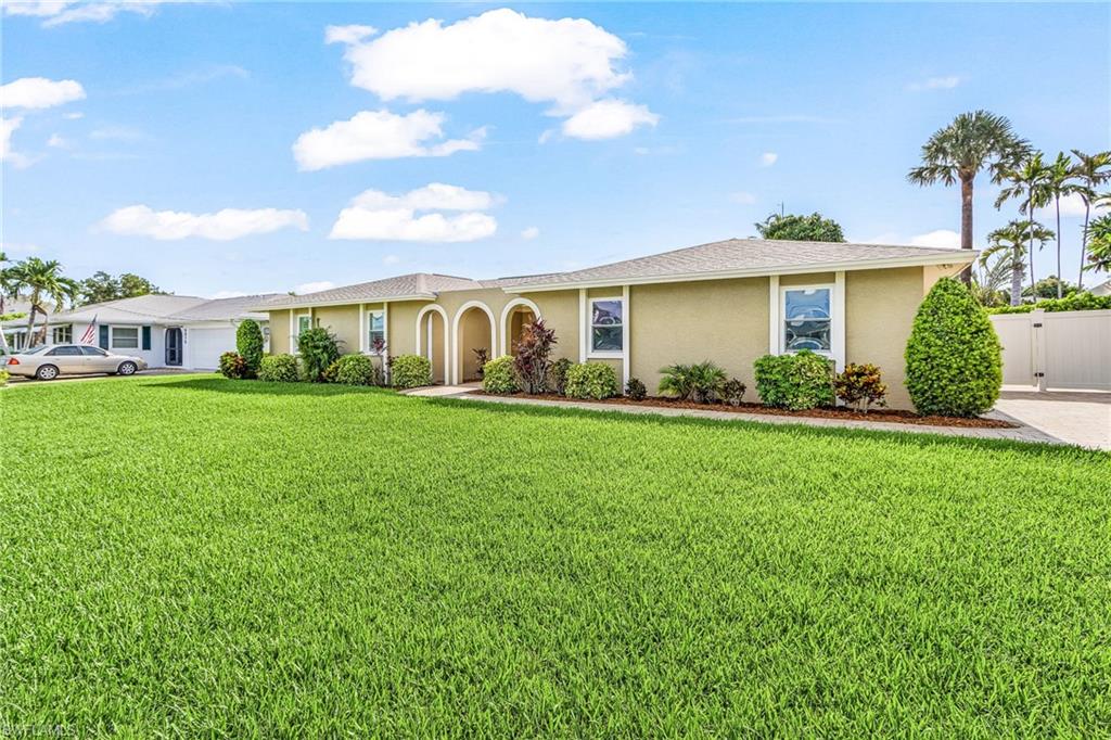 Spacious front lawn with mature landscaping, stucco exterior, arched entryways, white-framed windows, and a privacy fence