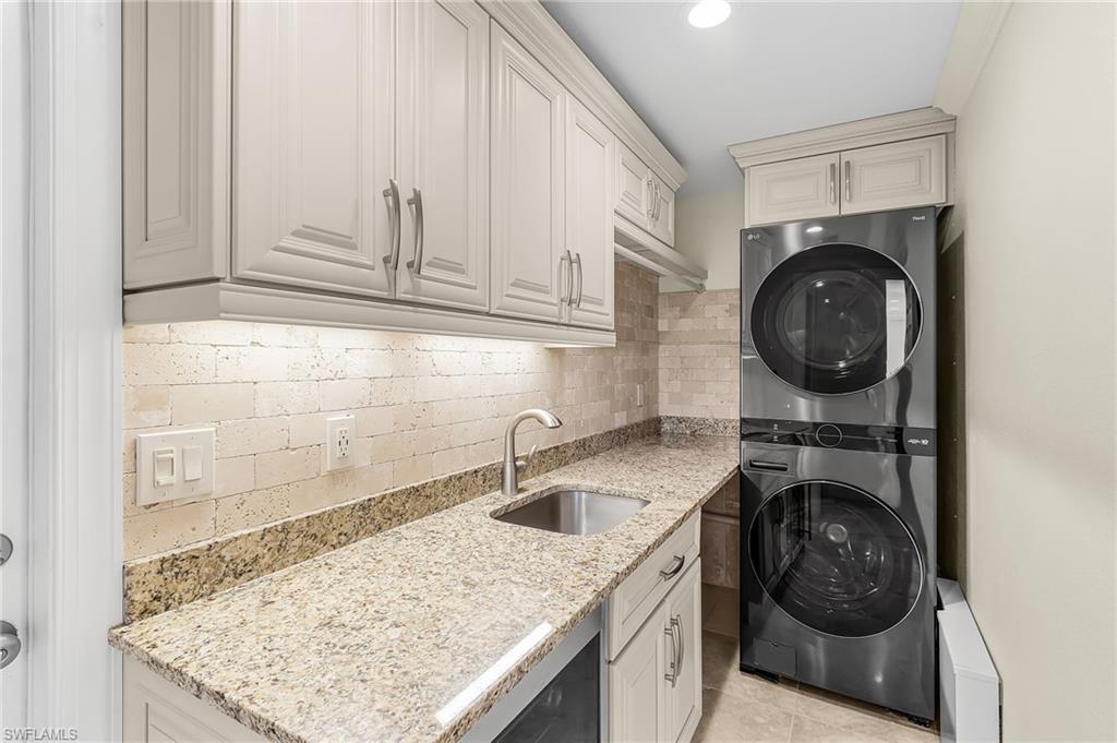 Laundry area featuring a built-in stainless steel sink, granite countertops, and stacked appliances