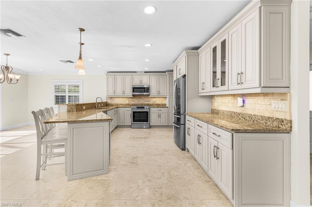 Spacious kitchen featuring a large breakfast bar, stone countertops, light-toned cabinetry, a built-in oven, and a French door refrigerator