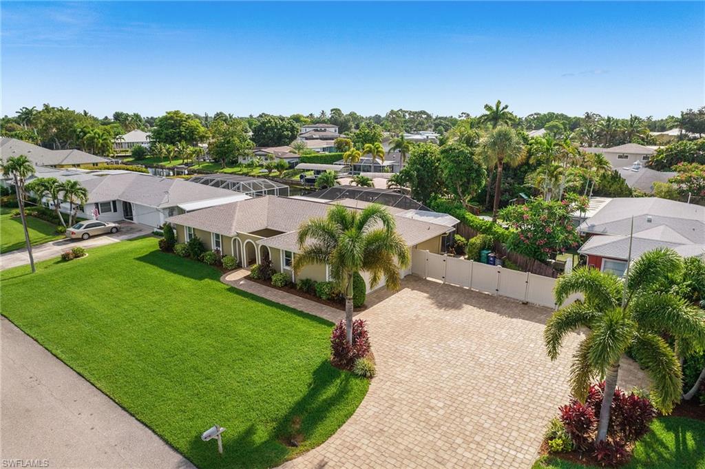 Exterior featuring a paver driveway, expansive front lawn, lush landscaping, and mature palm trees
