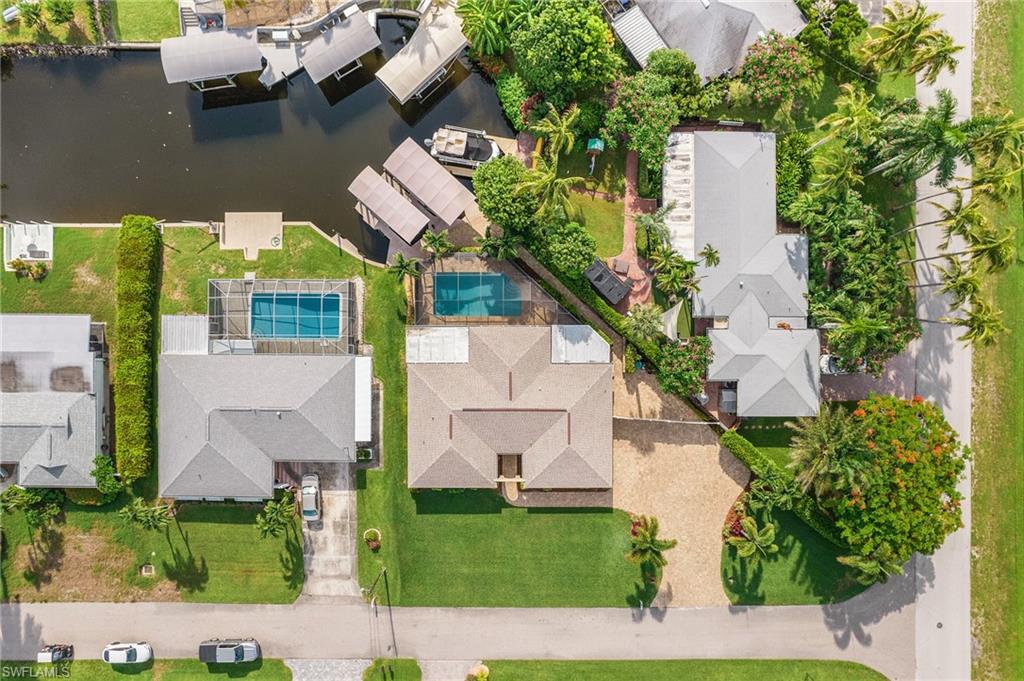 Aerial view highlighting a property with a gravel driveway, mature trees, and a manicured lawn