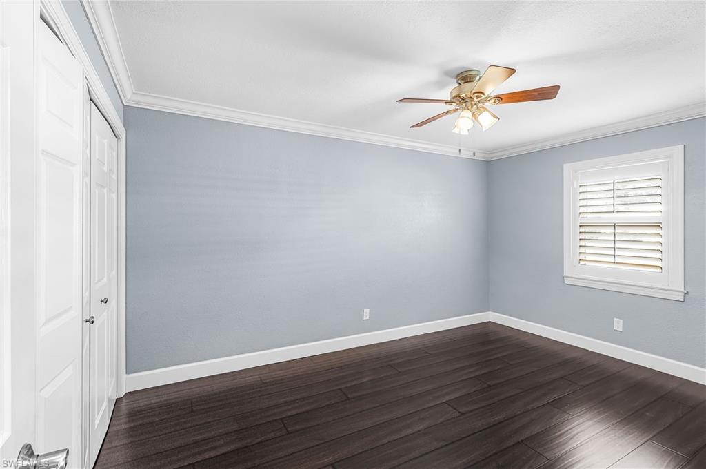 Spacious room featuring dark wood-finish flooring, light blue walls, and white crown molding
