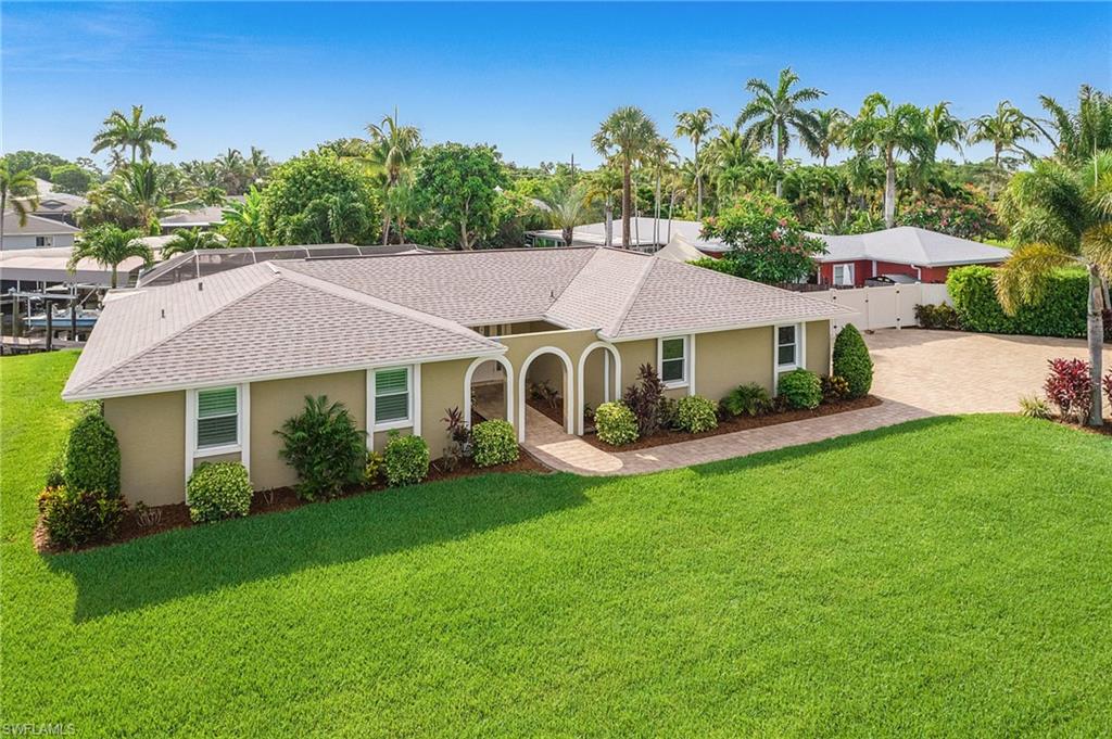 Stucco exterior residence with an arched entry, a light-colored shingle roof, and manicured landscaping