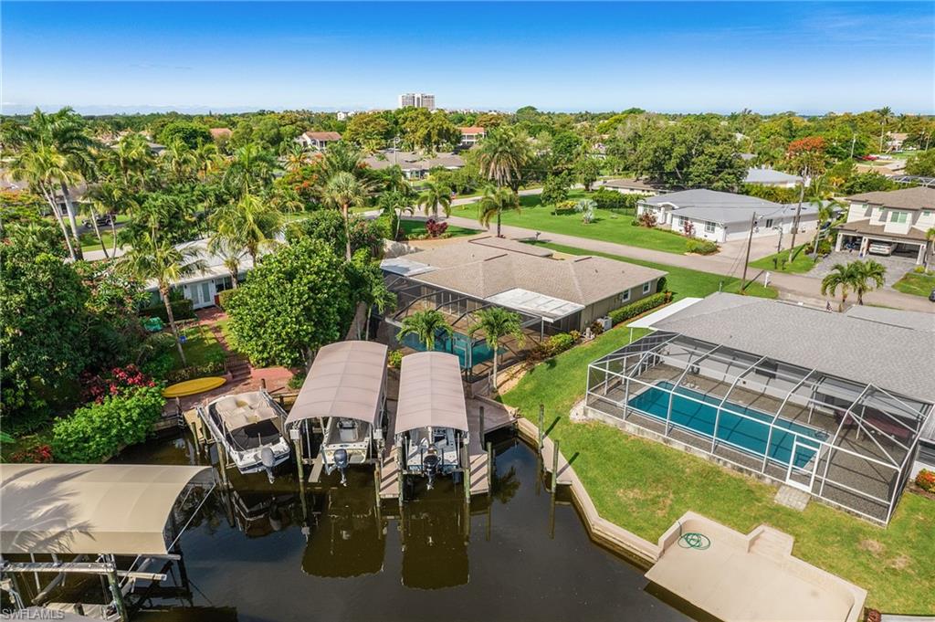 Waterfront property featuring multiple boat lifts with covered canopies, a screened swimming pool, and a lush, tree-lined landscape