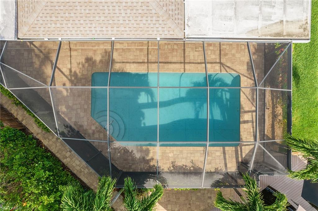 Screened swimming pool with integrated steps, surrounded by paver decking and mature landscaping