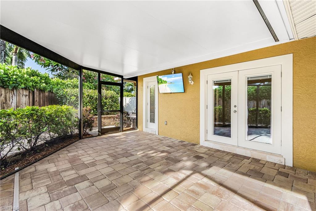 Screened outdoor living area featuring paver flooring, a flat ceiling, and two sets of glass-paned French doors
