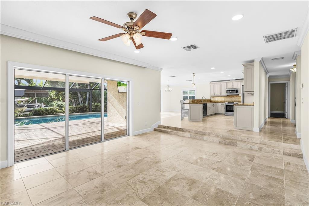 Spacious interior with neutral tile flooring throughout, featuring large sliding glass doors opening to a screened pool area with paver decking