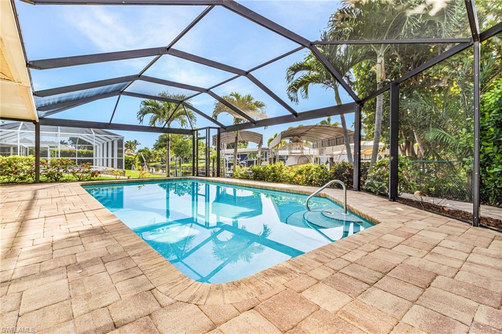 Screen-enclosed swimming pool featuring a paver deck, integrated steps, and a metal handrail