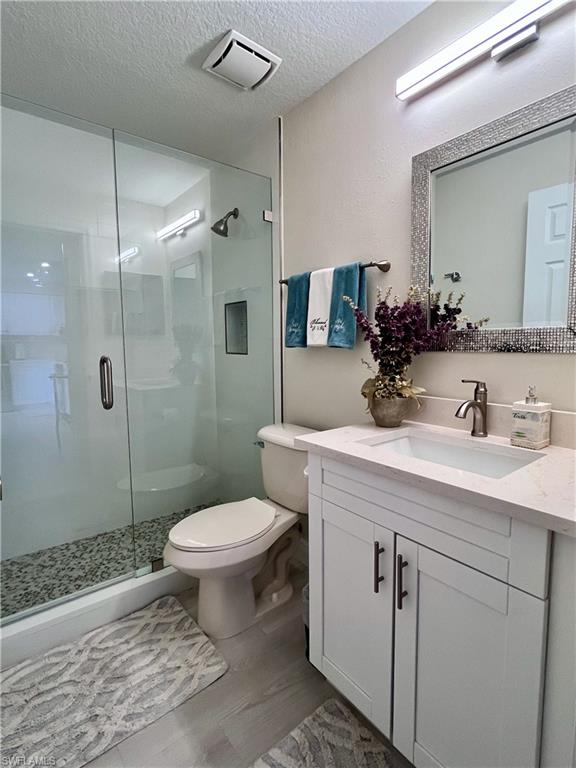 Full bath with a shower stall, vanity, a textured ceiling, and dark wood finished floors