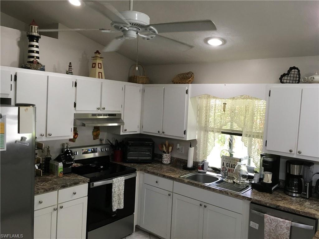 Kitchen featuring white cabinetry, stone-look countertops, stainless steel appliances, a double basin sink, and a ceiling fan with integrated lighting