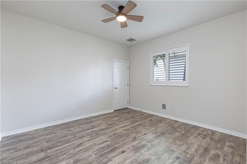 Interior room featuring wood-finish flooring, a ceiling fan with integrated lighting, and a window with white plantation shutters